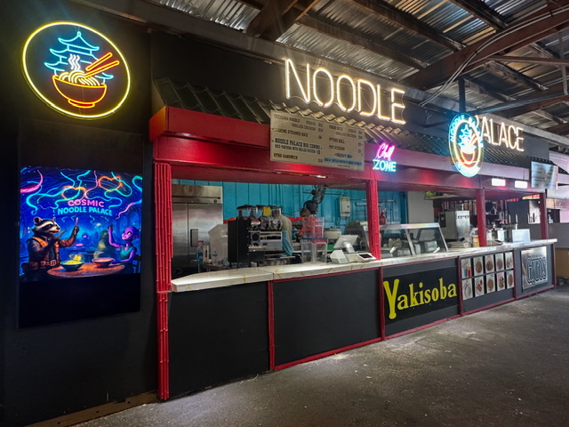 Noodle Palace booth at night — neon signs glowing